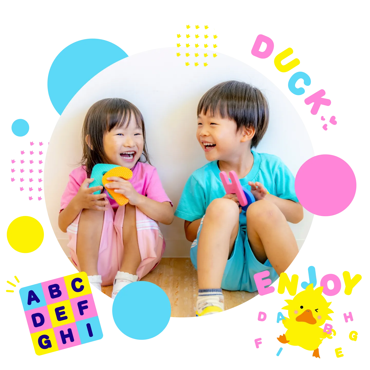 ピンクと水色の服を着た2人の子どもが、カラフルなアルファベットのおもちゃを手に持ちながら座り、向かい合って笑い合っている丸い写真。写真のまわりには「DUCK」「ENJOY」などのカラフルな文字や、ダックのイラスト、アルファベットの装飾が散りばめられている。